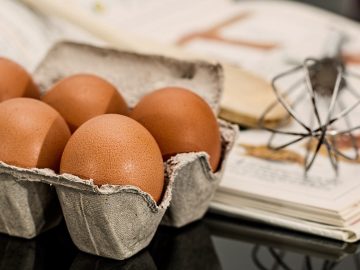 oeufs, fouet et livre de recettes posés sur une table