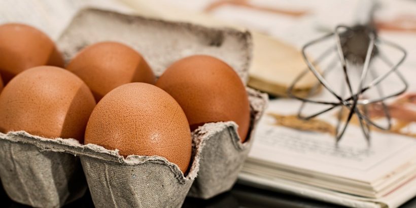 oeufs, fouet et livre de recettes posés sur une table